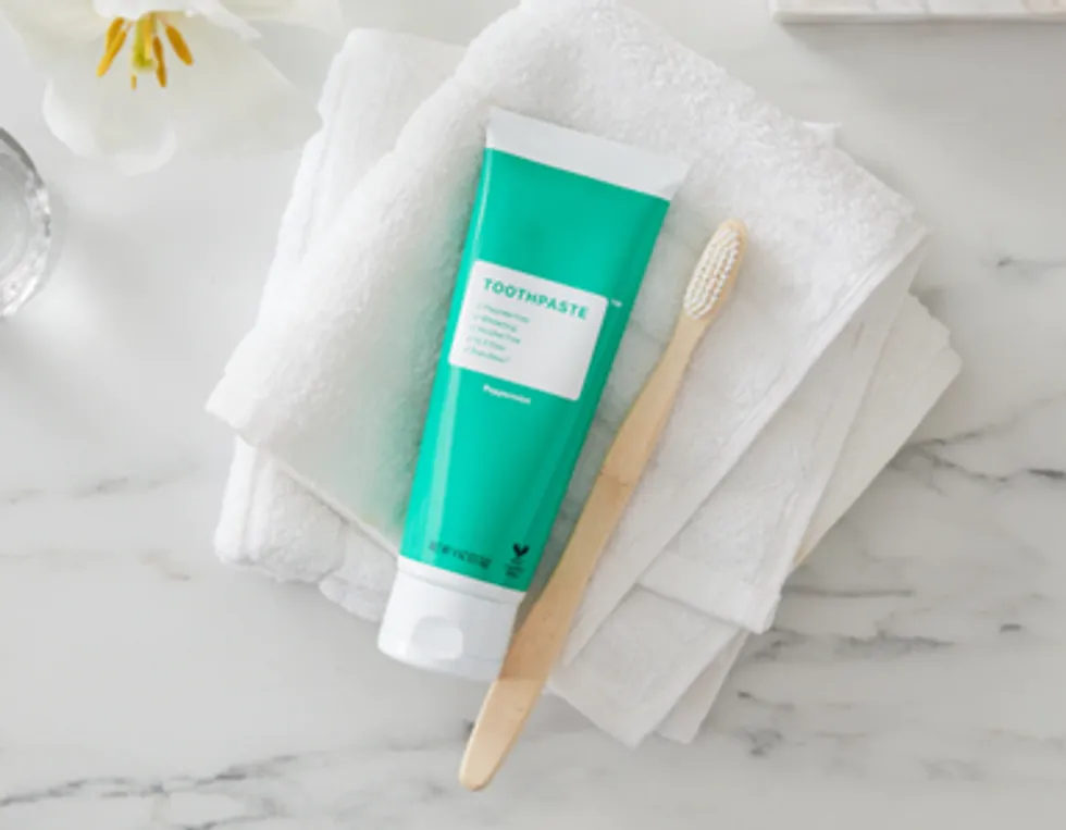 Editorial image of a mint-green toothpaste tube and bamboo toothbrush arranged on a white towel